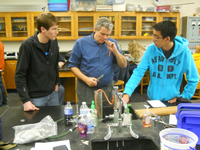Stephen Clark (center), using a graduated cylinder, a small hose, water, and a tuning fork, shows seniors Chris Pham (right) and Jeremiah Smith (left) how musical instruments generate sounds and vibrations.