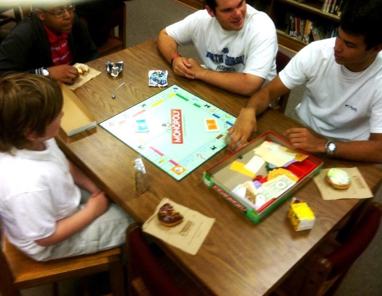 Seniors Garrison Elliot and Hayden Beyer mentor Oak Grove Elementary students by challenging them to a game of Monopoly.
