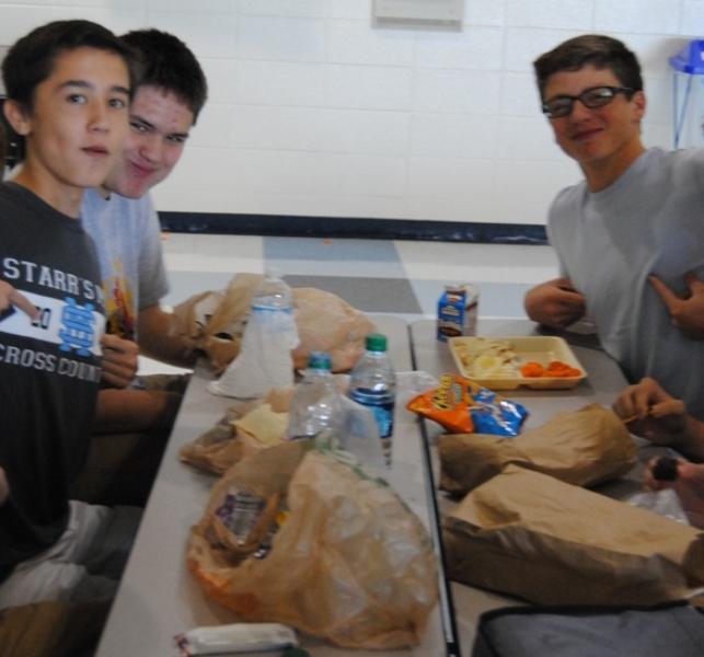 Sophomores Connor Donahue ( far left)  and Jake Odom (left), eat their filling sack-lunches during B lunch. Nick Palmer (right) eats a school lunch consisting of garlic French bread pizza, some  carrots, and a bag of Cheetos.