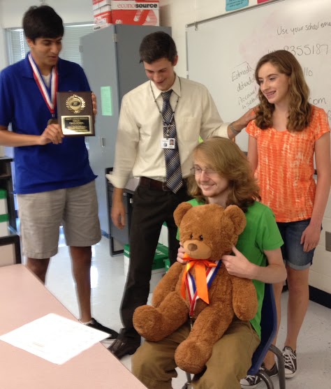 Debaters junior Aasim Noorali  (left), senior Michael Robinson (seated), and sophomore Aubrey Bennett  (right) celebrate a recent win with their coach Brandon Kendall. 