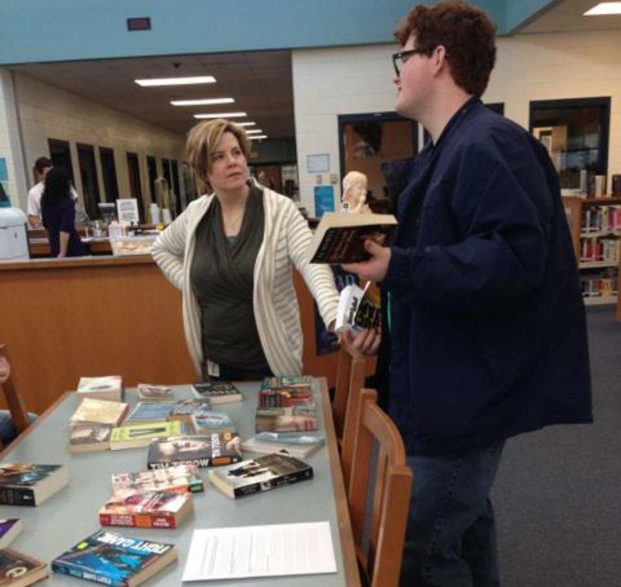 LeighAnne Hanie discusses the books at the book swap during Feed Your Need to Read week with senior Mac Price.