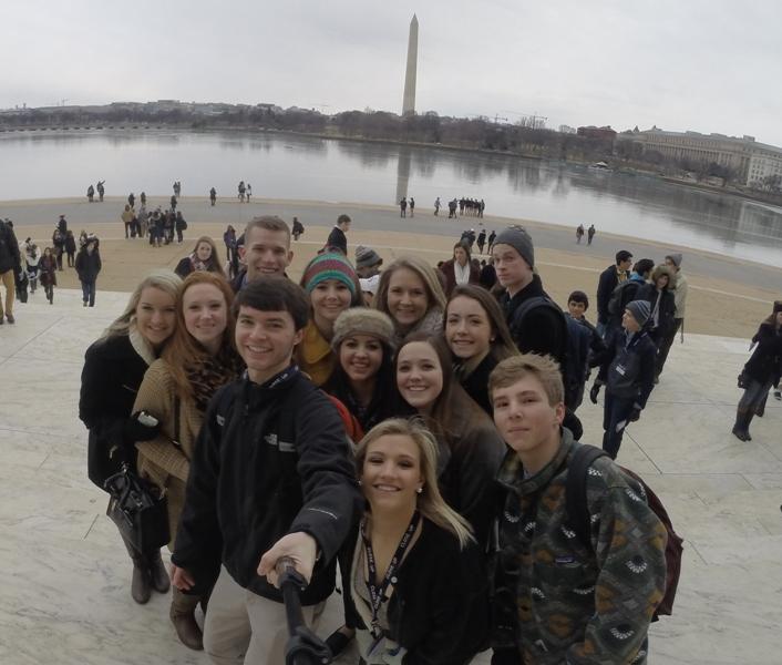 Students stand on the steps of the Jefferson Memorial where the Washington Monument can be seen in the distance.