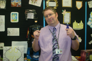 English teacher Shad Genovese proudly stands in front of a giant Batman figurine. He holds Batman and Joker action figures. 