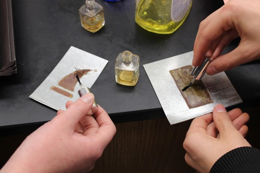 Dec. 4, 2015 - Dan Gant’s chemistry students create Christmas ornaments out of steel, tape, and acid to make rust designs. These students are painting over their rust with clear nail polish to prevent it from chipping away.