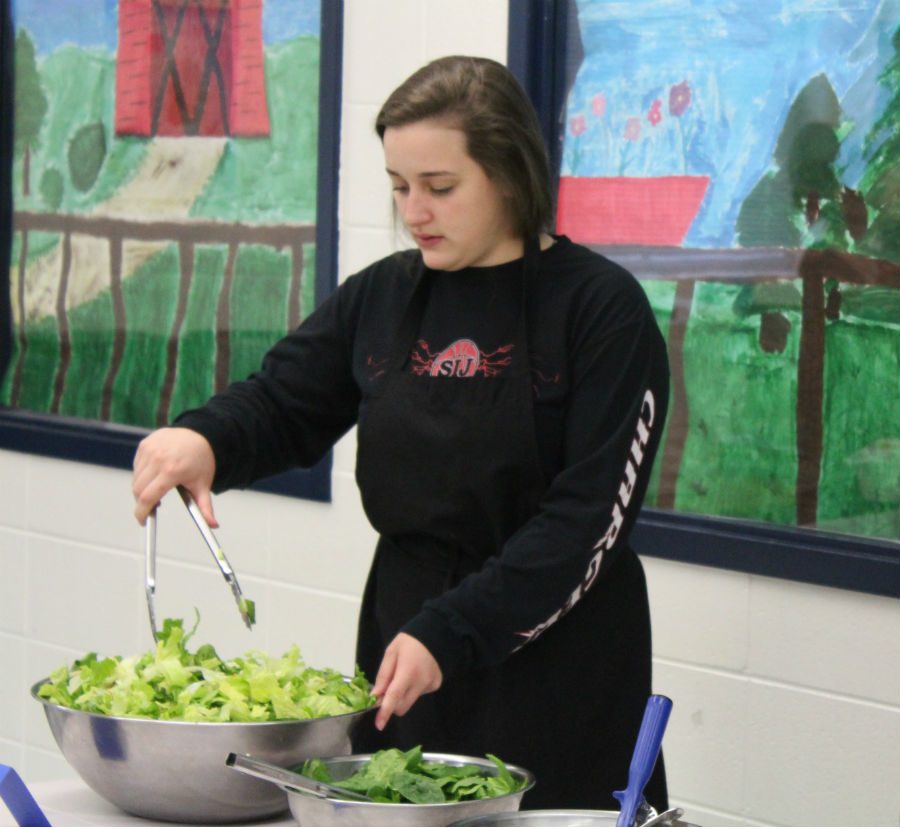 Culinary+arts+student+works+the+salad+bar+the+week+before+spring+break+at+%E2%80%9CSalads+and+Spuds%2C%E2%80%9D+a+faculty+luncheon+set+up+by+nutrition+and+wellness+teacher+Cheryl+Clower.+Students+gave+a+survey+to+40+teachers+to+create+the+menu%2C+and+teachers+spent+%247+for+their+meal.+