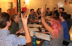 The entire cast and crew of The Last Night at Ballyhoo, seniors Kade Smith, Nora Bill, Rollin Rocket, Noah McPherson, Avery Grillo, Walker Allen, Zabrina Corrales, junior Ginni Gray, and sophomore McKenna Rockwell, hold up “focus foxes” in order to gain everyones attention before beginning the script. The cast and crew sit down for the first table read of the competitive one act play that will be performed at Whitewater High School on Oct. 22. 