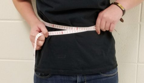 A student measures her waist. Students are pressured with the unrealistic expectation to have a smaller-than-average waist and body frame.