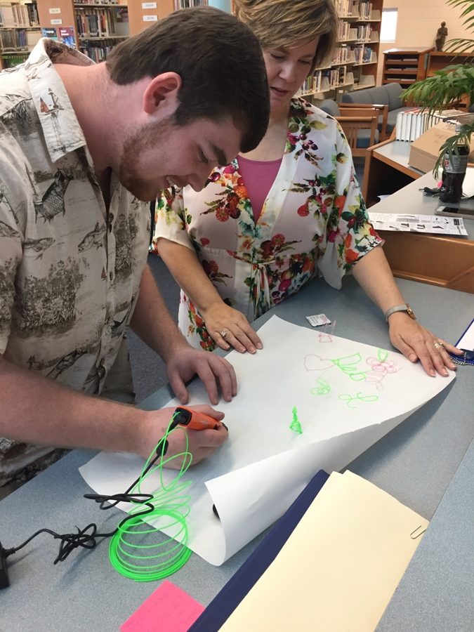 Media center specialist Leigh Anne Hanie assists a student using the 3D printer pen in the Makerspace cart.