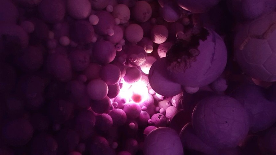 A light emits from the purple sports ball cavern in Arsham’s installation. The question of the origin of the many idiosyncratic objects becomes the quest of the viewer.