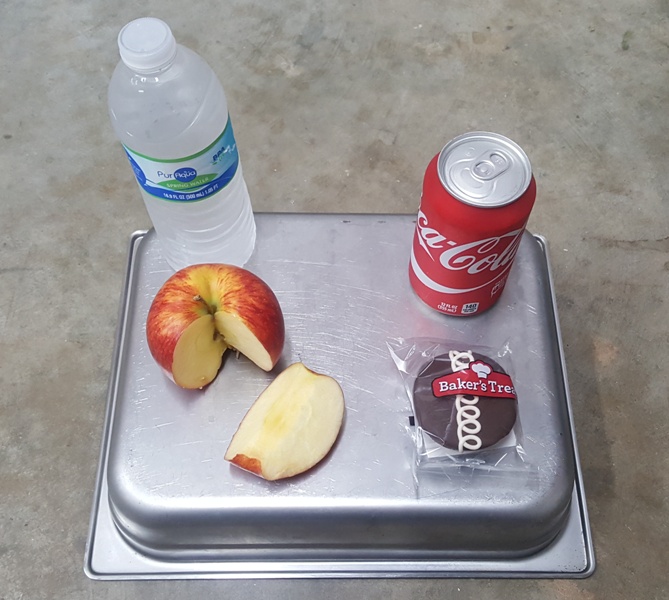 An unhealthy snack option of a cupcake and a Coke placed next to the healthy alternative of an apple and a water. Decisions between these two snacks are hard to make, because students value taste over nutrition. 