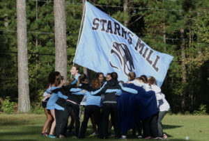 A junior from the varsity boys’ cross country team runs the team flag around members of the girls’ team as the varsity girls prepare for their race at their region meet on Oct. 21. The Lady Panther runners ended with three girls placing in the top ten individually and second in the region. 