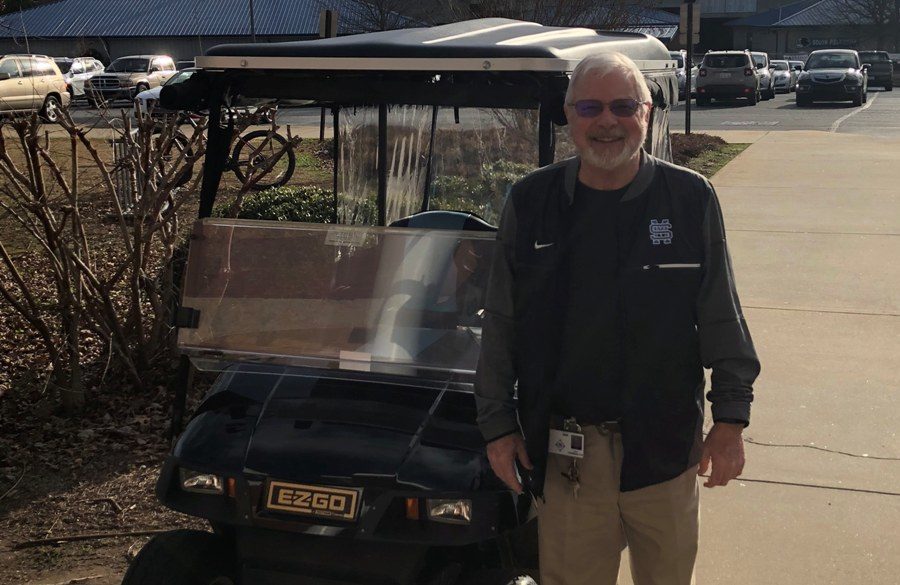 Fred Harrington outside of the attendance office with the parking lot golf cart. Harrington just started his job as parking lot attendant after working with the school for more than 10 years.