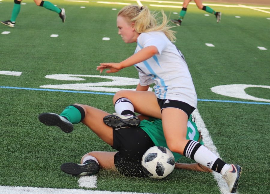 Junior Meritt Parker trips over a Lady Chief as she attempts to dribble the ball. The Mill lost to their crosstown rival McIntosh 4-2 in penalty kicks.