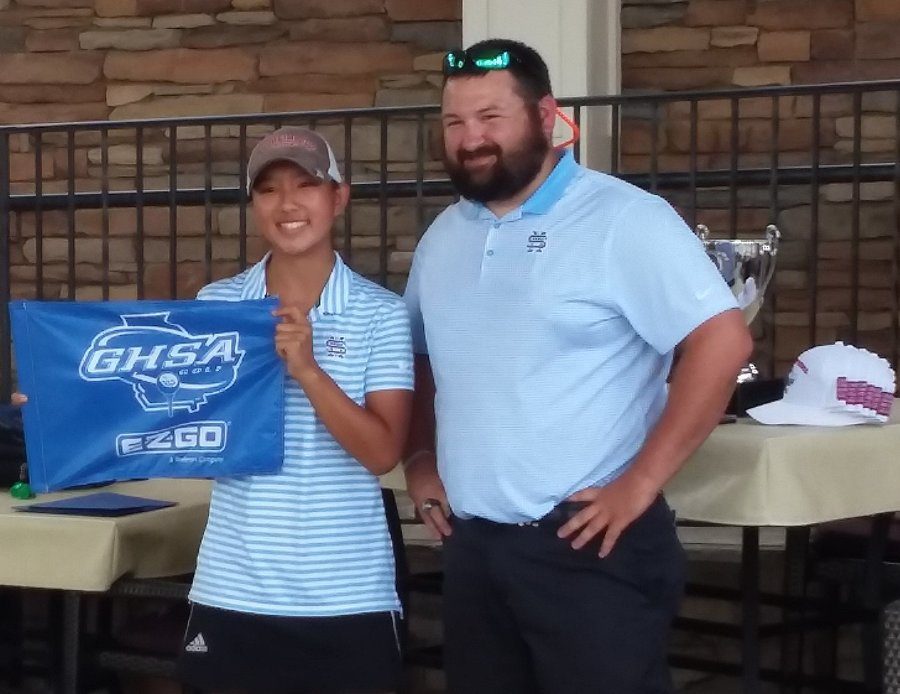 Junior Liza Eubanks holds a banner with the logo for the GHSA state tournament. Eubanks led the Mill, finishing seven strokes ahead Sutton Rollins from Ware County. Overall, the girls’ team won by 28 shots for their second straight AAAAA state title. 