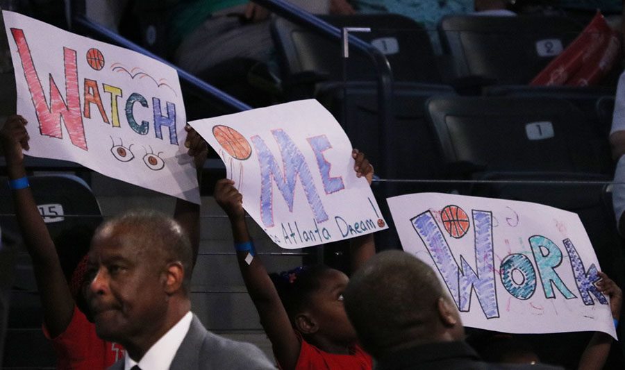 Three young girls display signs with one of the Atlanta Dream mottos. Several players own businesses or support causes outside of the WNBA, helping them serve as role models on and off the court.