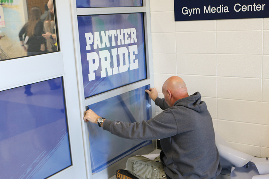 Dec. 11, 2019 - Maintenance worker places a blue cover onto the glass doors by the attendance office. These doors, along with the ones by the front office, are a new security addition to the school this year.