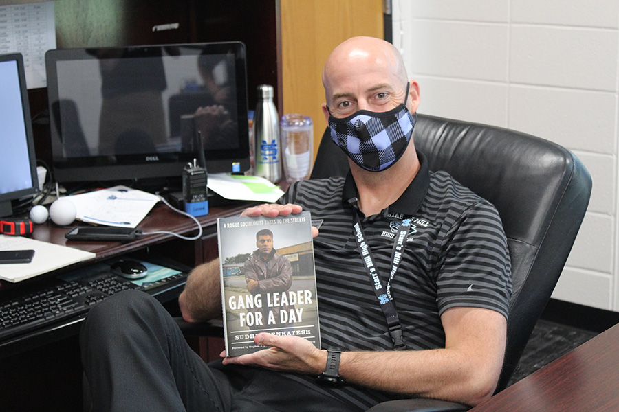 Principal Allen Leonard sits at his desk with “Gang Leader for a Day” by Sudhir Venkatesh. The book goes through a sociological study focused on the function of Chicago street gangs within the urban poor societies.