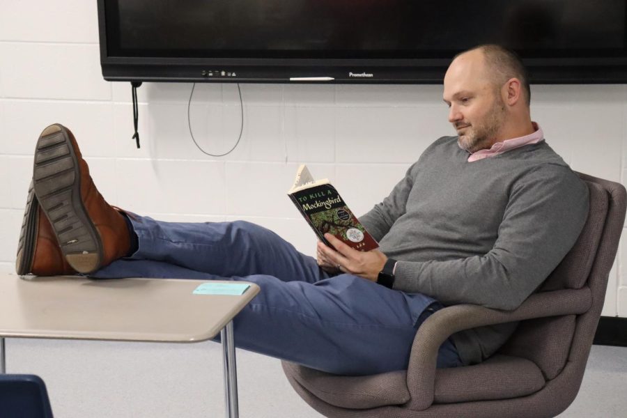 U.S. history teacher and varsity boys basketball coach Joshua Reeves sits at his desk with “To Kill A Mockingbird” by Harper Lee. The book focuses on racism in the 1930s and how a small family navigates the struggle between right and wrong in the South.
