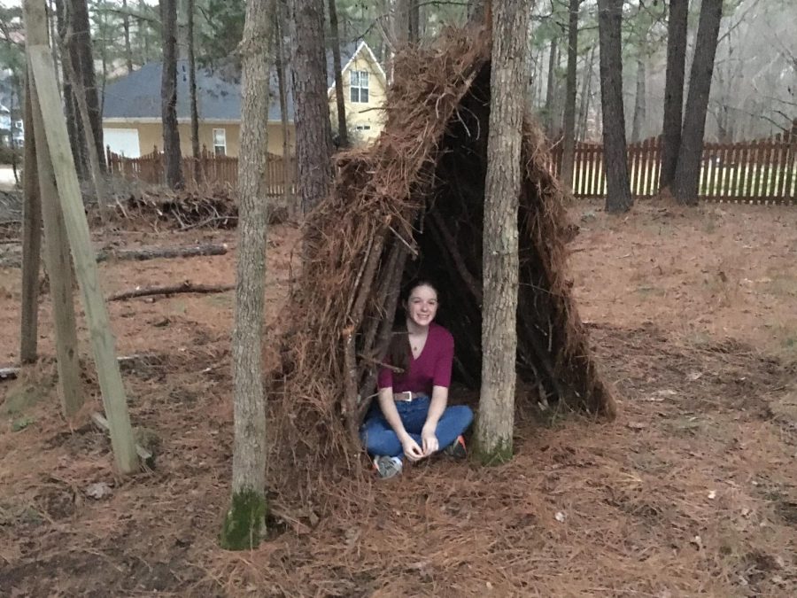 Sitting in a survival shelter I made in my backyard. Survival shelter building is one of many essential skills students could learn in a course designed to help with emergency preparedness.