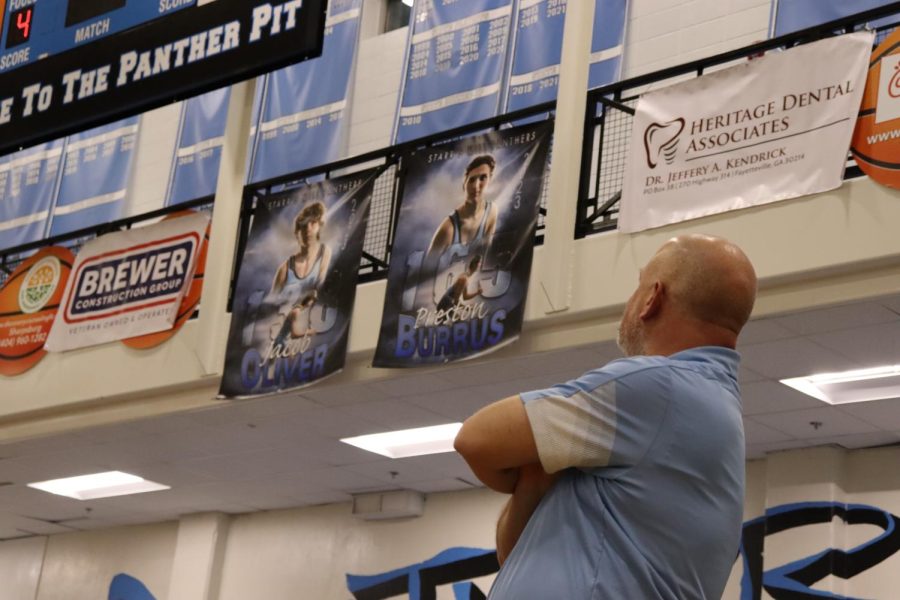Wrestling head coach John Steiner looks up at the posters for the team’s two seniors, Preston Burrus and Jacob Oliver. “Our two seniors are captains. They take on roles like starting the drills, starting the warmups, and if the guys aren’t working as hard as they should be they’re the motivators to get those guys going,” Steiner said.