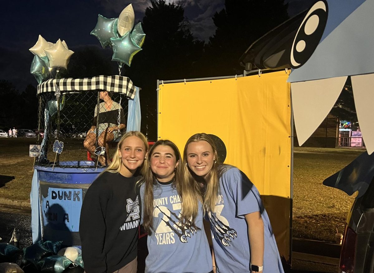 The+swim+teams+set-up+for+Trunk+or+Treat.+They+set+up+a+dunk+booth+and+gave+out+candy.+Junior+Jacob+Ramsey+is+in+the+dunk+booth%2C+and+seniors+Emma+Frank%2C+Sophia+Cochran%2C+Caroline+Craddock+are+helping+run+the+station.+