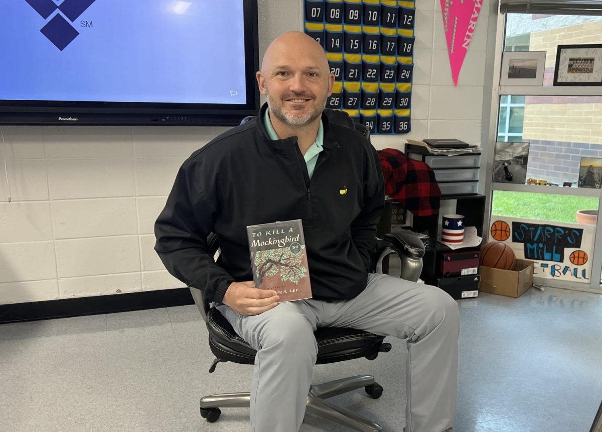 Social+studies+teacher+Joshua+Reeves+holds+his+favorite+book%2C+%E2%80%9CTo+Kill+A+Mockingbird%2C%E2%80%9D+by+Harper+Lee.+Reeves+read+the+book+for+the+first+time+in+high+school%2C+and+has+re-read+it+multiple+times+since.+